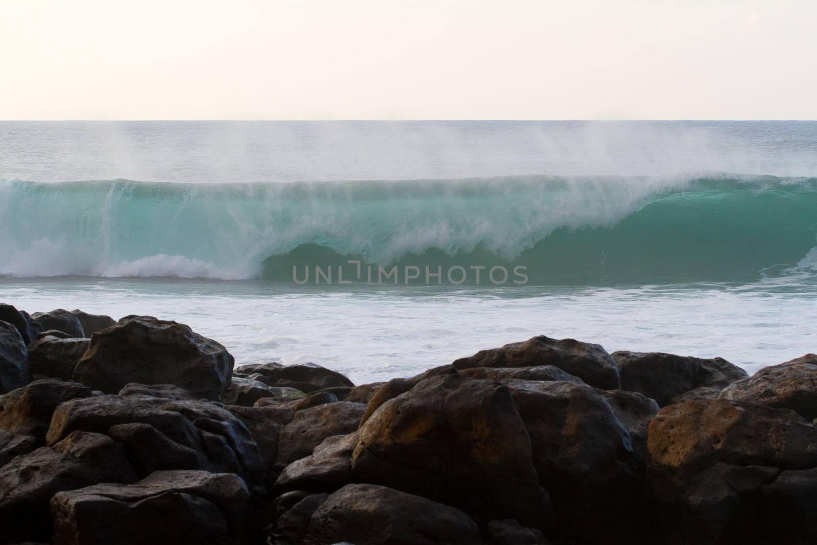 This huge wave breaks just beyond some rocks near pipeline on the north shore of Oahu in Hawaii during a big storm.