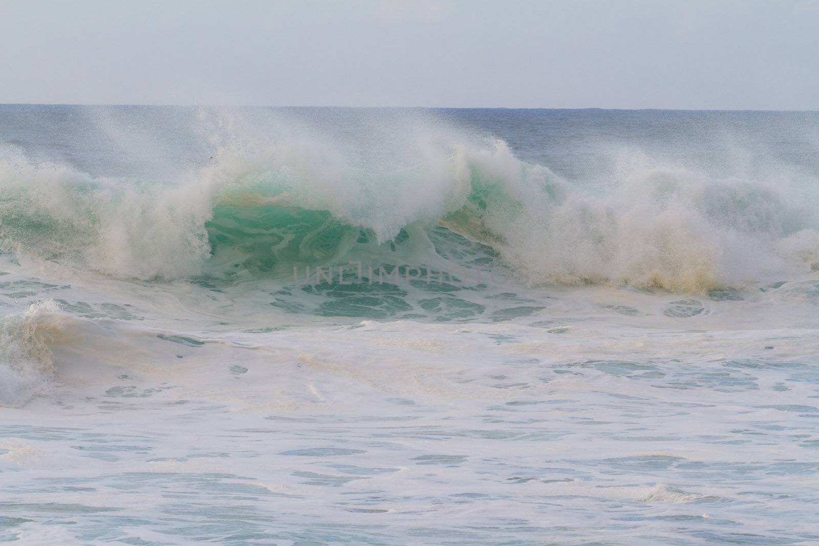 A giant wave breaking during a storm on the north shore of Oahu in Hawaii. These incredible waves have tons of white water and froth with hollow barrels and a dangerous rip current.