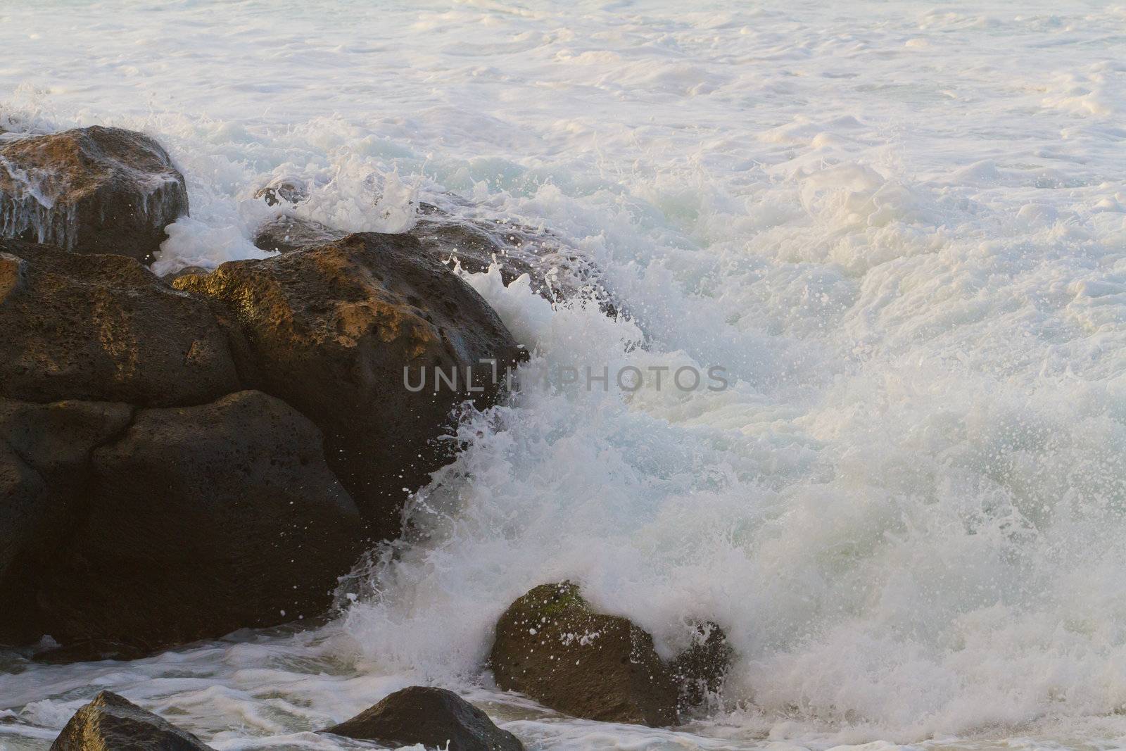 White frothy water rushes in dangerously over some rocks on the north shore of Oahu during a huge storm in the ocean.