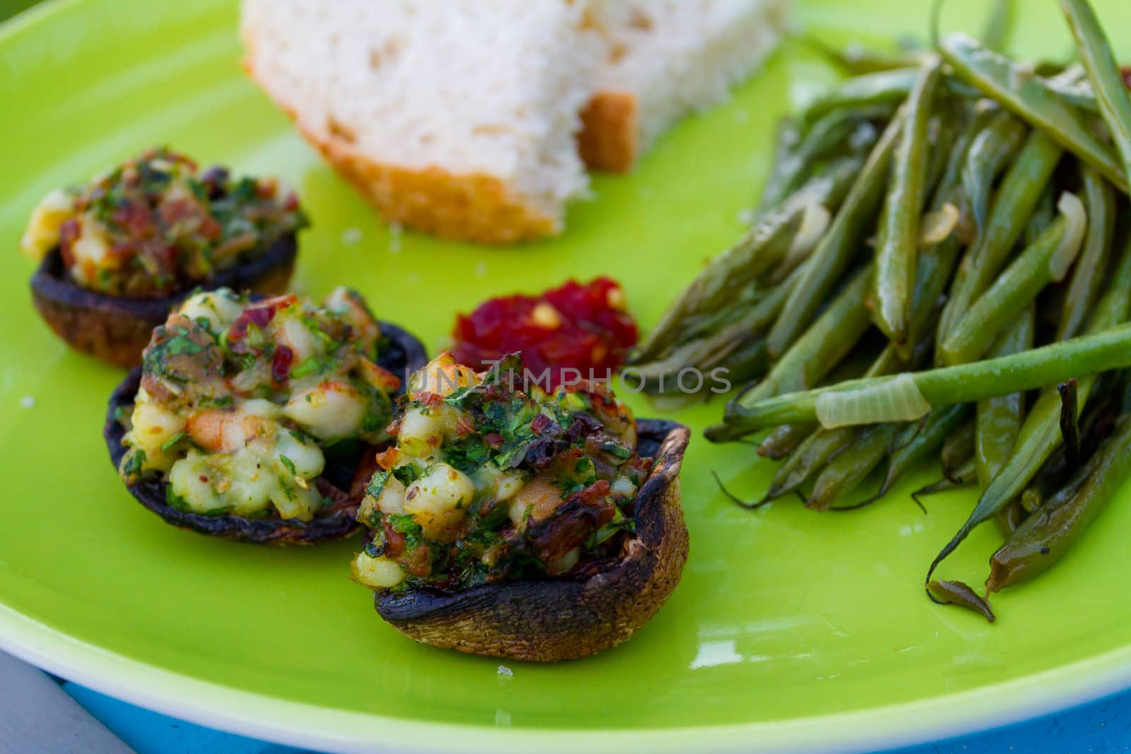 This gourmet meal of stuffed mushrooms and green beans served on a green plate with some white bread. This is dinner but the image applies to lunch also.