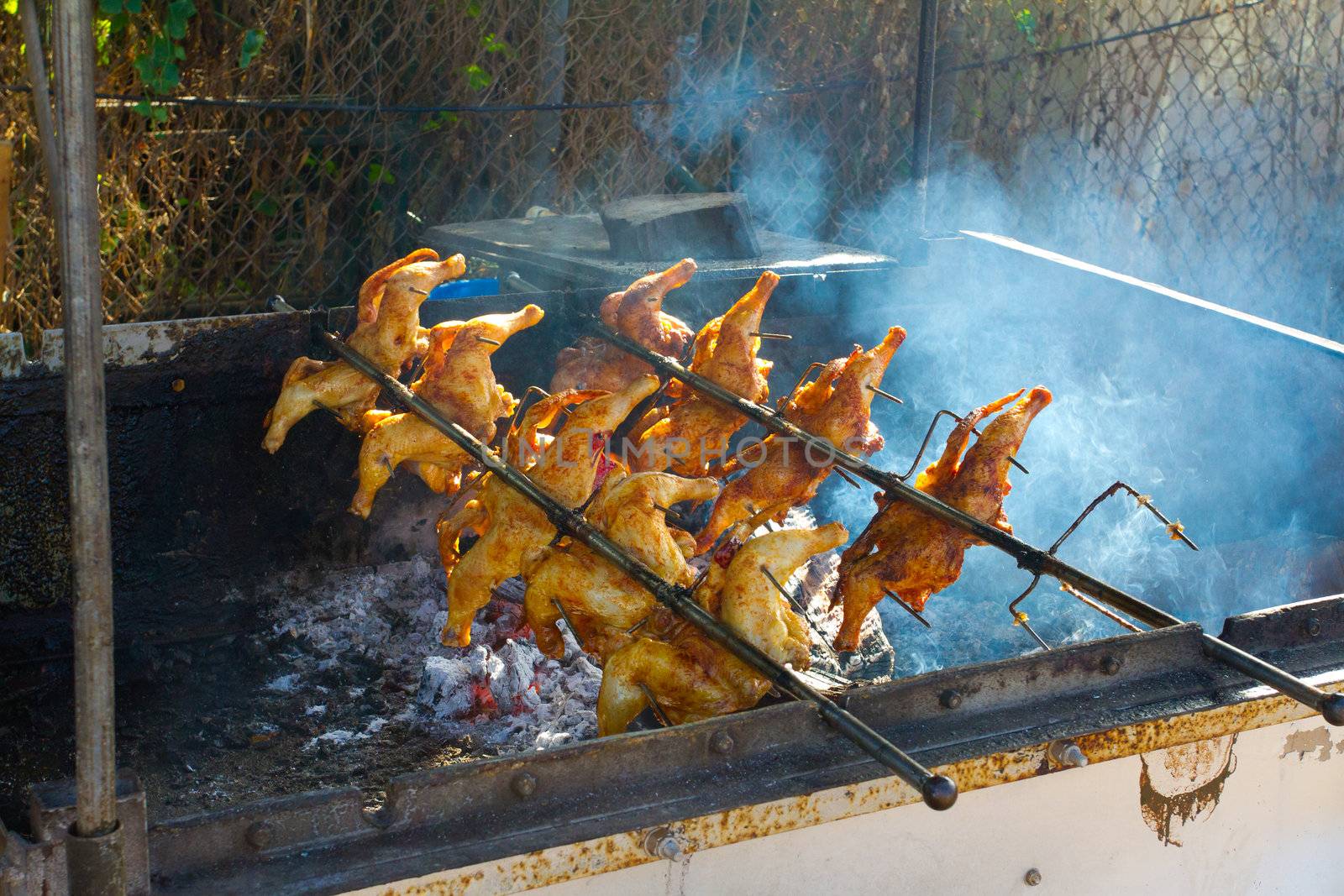 Barbeque chicken is being cooked over a wood fire with a rotisserie in Hawaii for lunch plates.