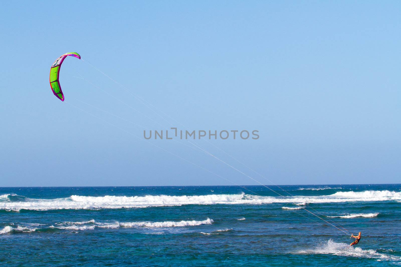 A man kite surfing in the waves along the north shore of Oahu. The kite is high above in the sky with plenty of wind to propel the man through the water on his surf board.