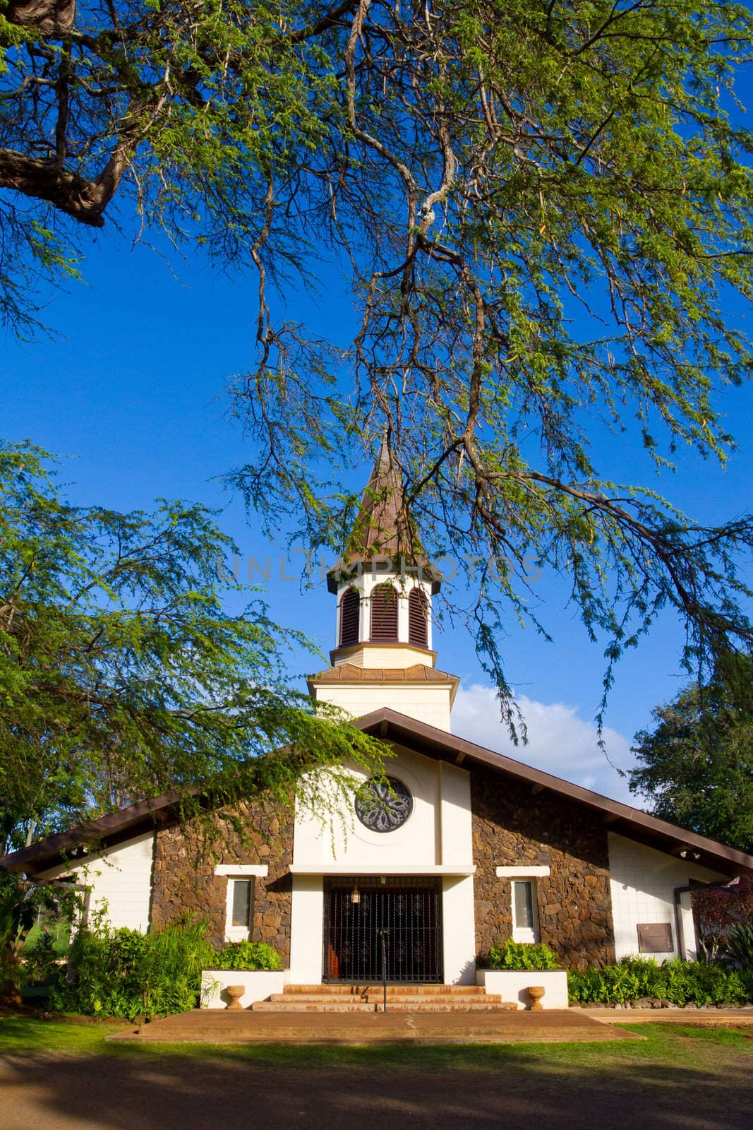 A beautiful old church in Haleiwa Oahu Hawaii exists among the tropical plant life and blue sky.