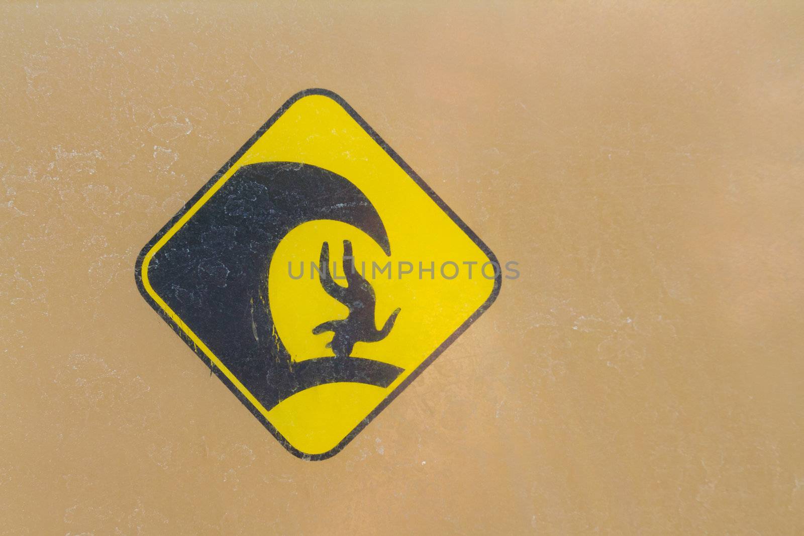 A warning sign for big waves has a simple weathered icon of a person upside down with a large surf wave crashing down on them.