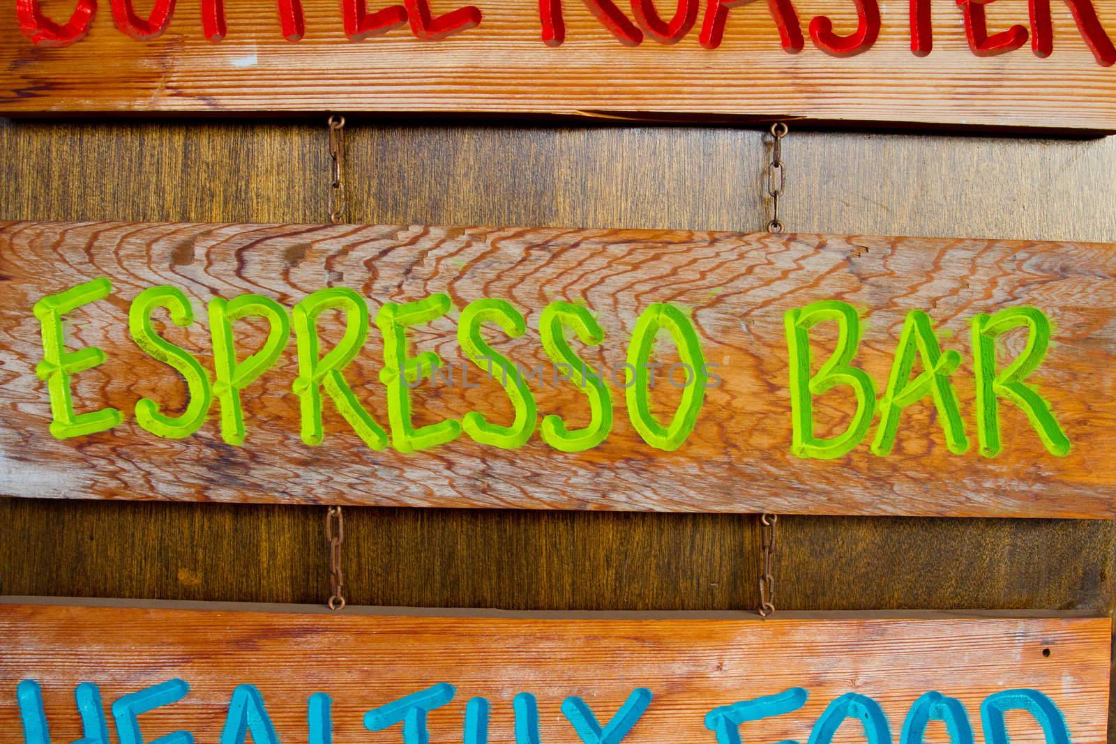 A handmade wood sign on a wood background is carved out and painted showing the words espresso bar in green letters.