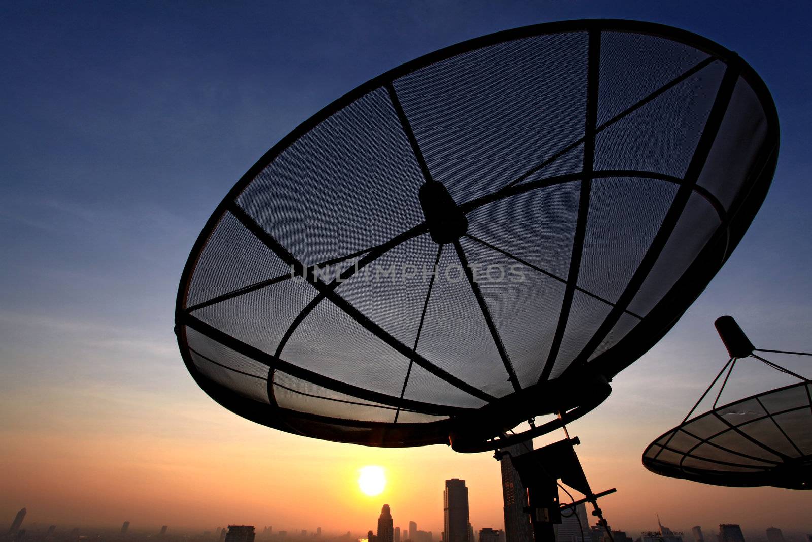 black antenna communication satellite dish over sunset sky in cityscape