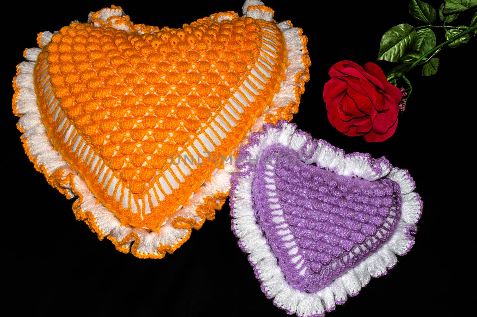 Two pillows in the shape of a heart and a flower rose on a black background.
