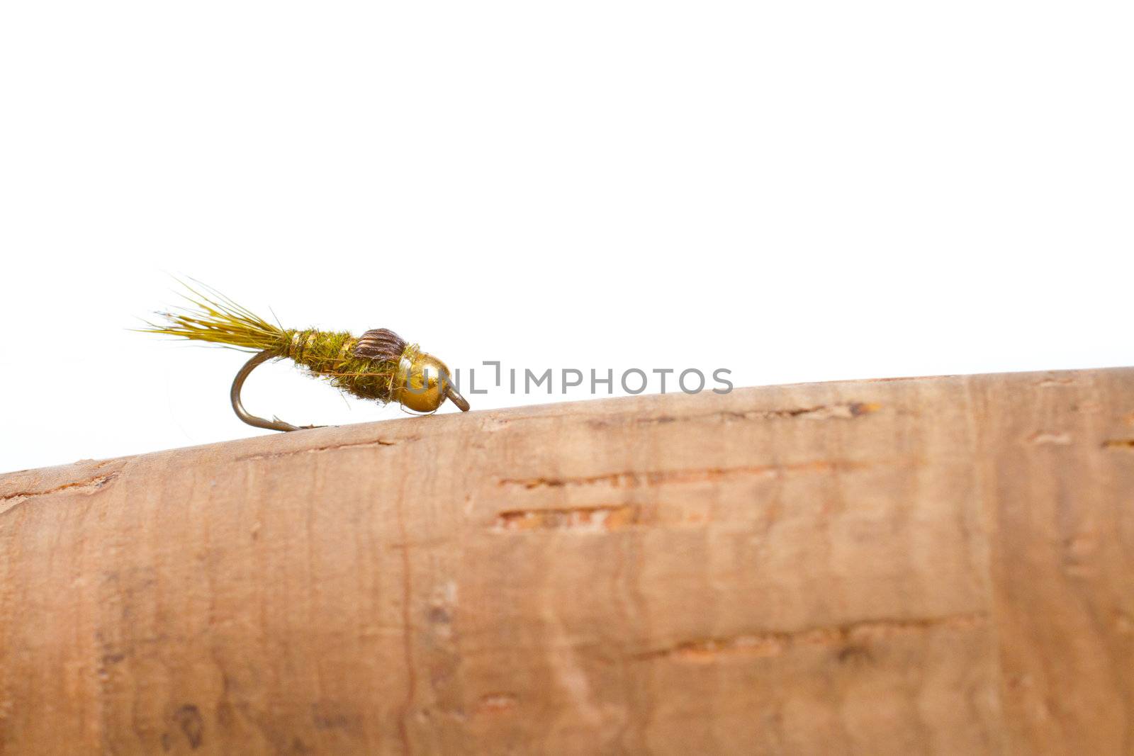 Isolated in a studio with a white background a hares ear nymph in natural colors is photographed closeup against the cork handle of a fly fishing rod.
