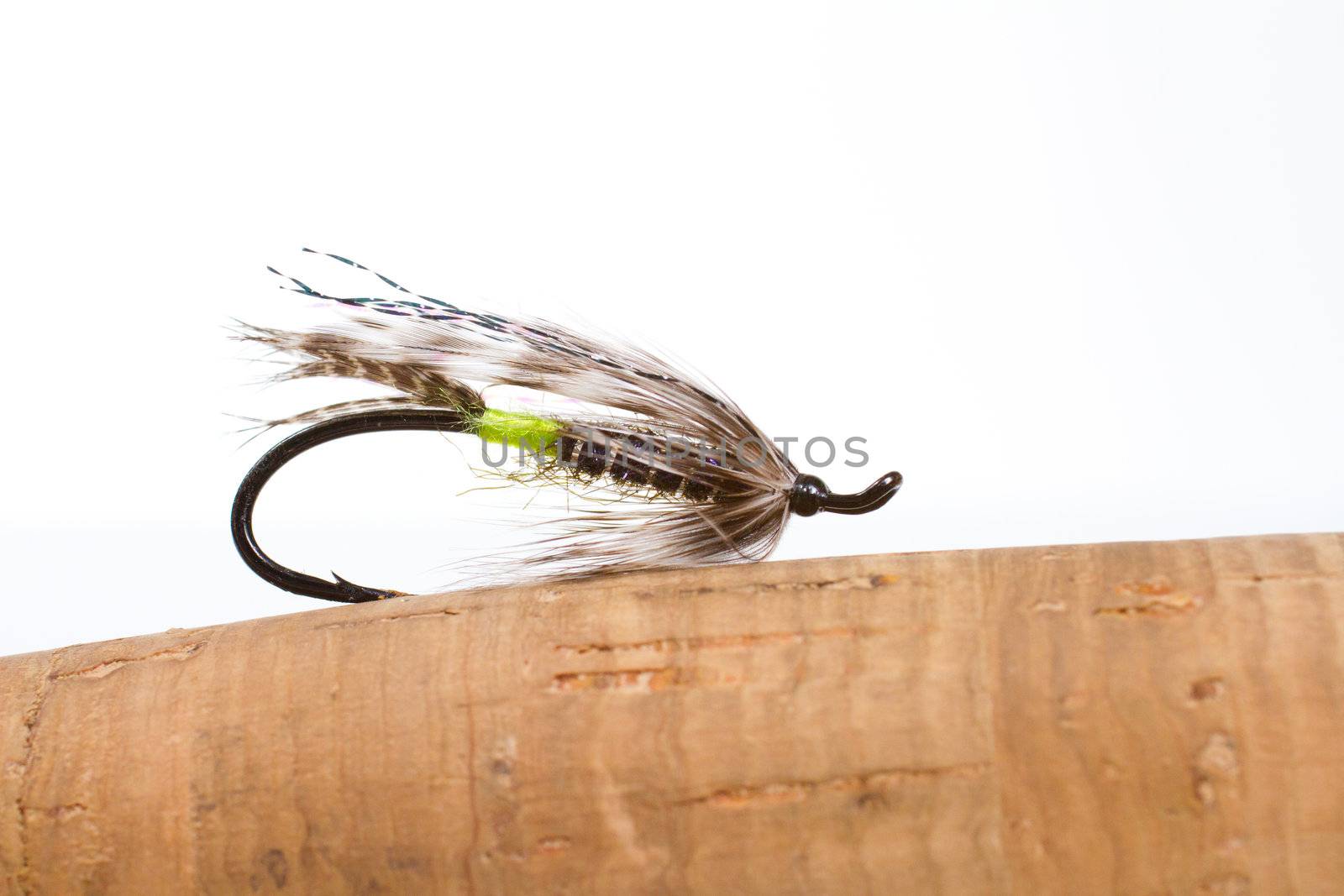 This green butted silver hilton steelhead fly fishing streamer is isolated against a white background in the studio along with the cork handle of the fly fishing rod.
