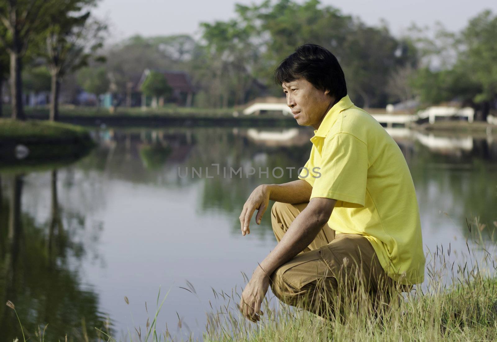 Middle age asian man sitting in the park by lake