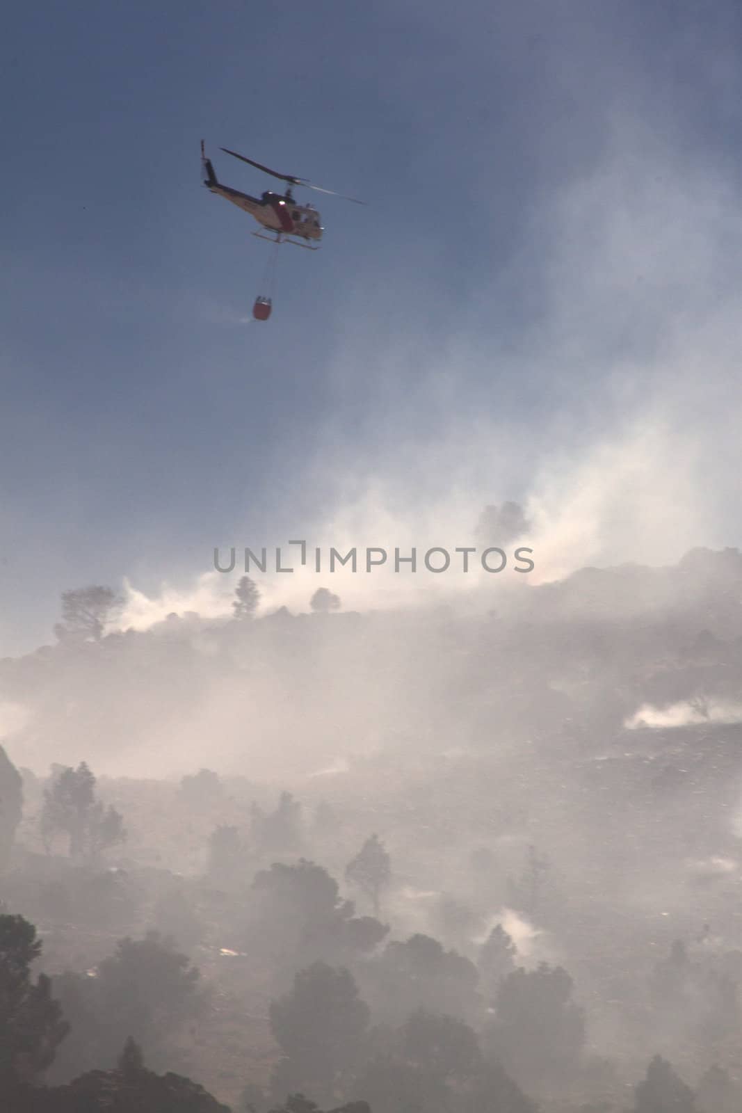 Fire fighting helicopter with smoke and the hillside by jeremywhat