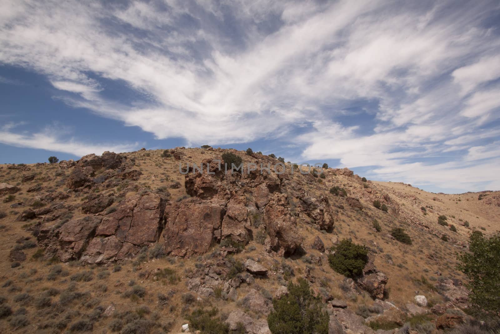 High deset rocky hillside with blue sky and beautiful couds by jeremywhat