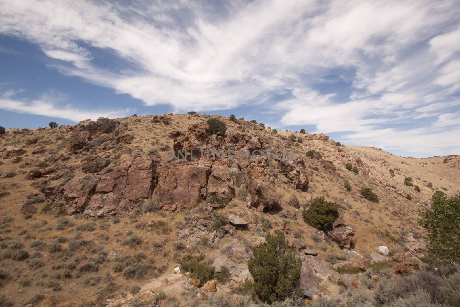 High deset rocky hillside with blue sky and beautiful couds by jeremywhat