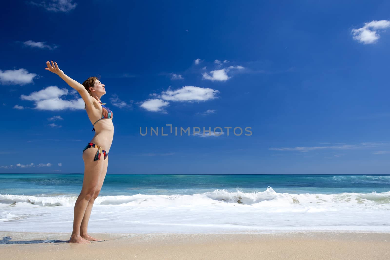 Beautiful young woman with arms open in a tropical beach enjoying the summer 