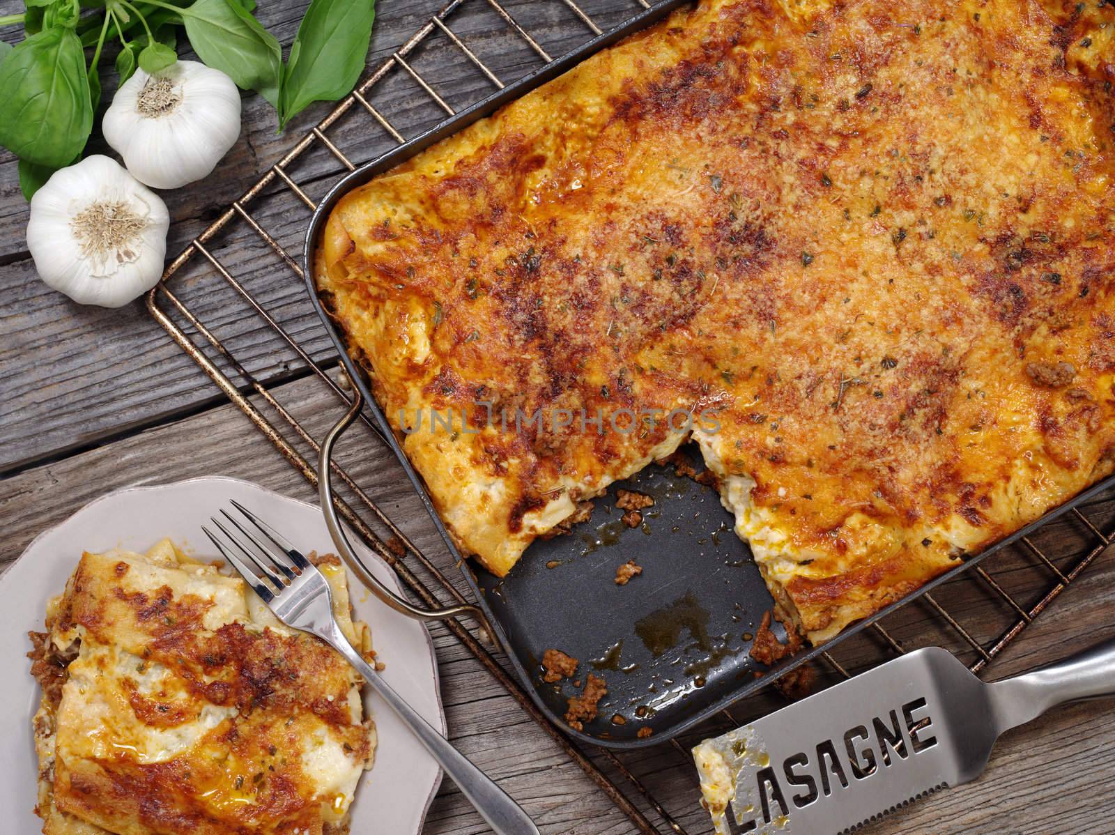 Photo of a freshly baked lasagna, sitting on an old wooden table with a portion cut out and waiting on a plate.