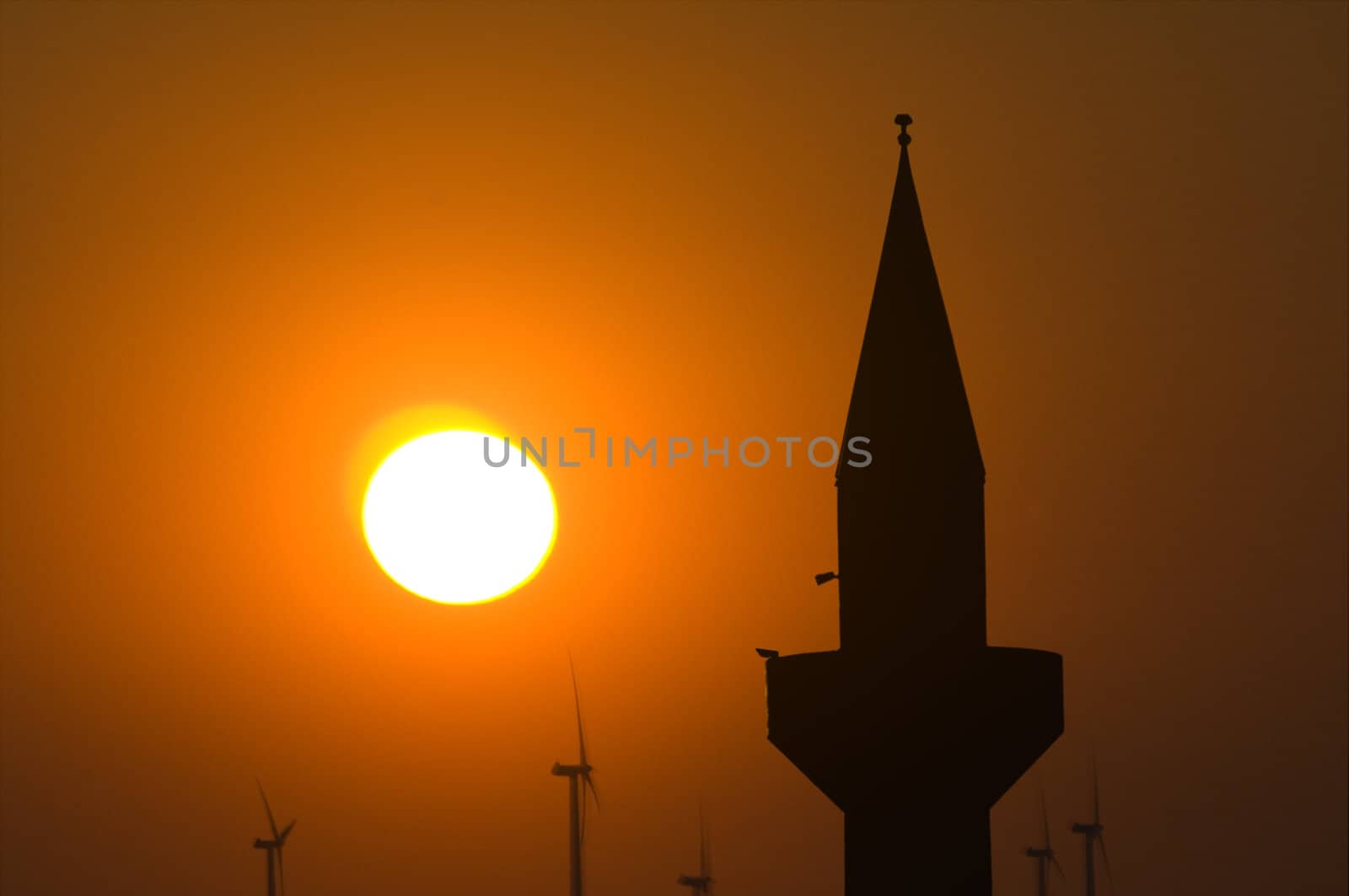 Minaret and wind turbines against a setting sun 