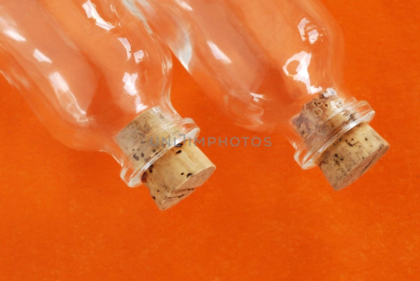 two small empty glass bottles closed with corks over orange background