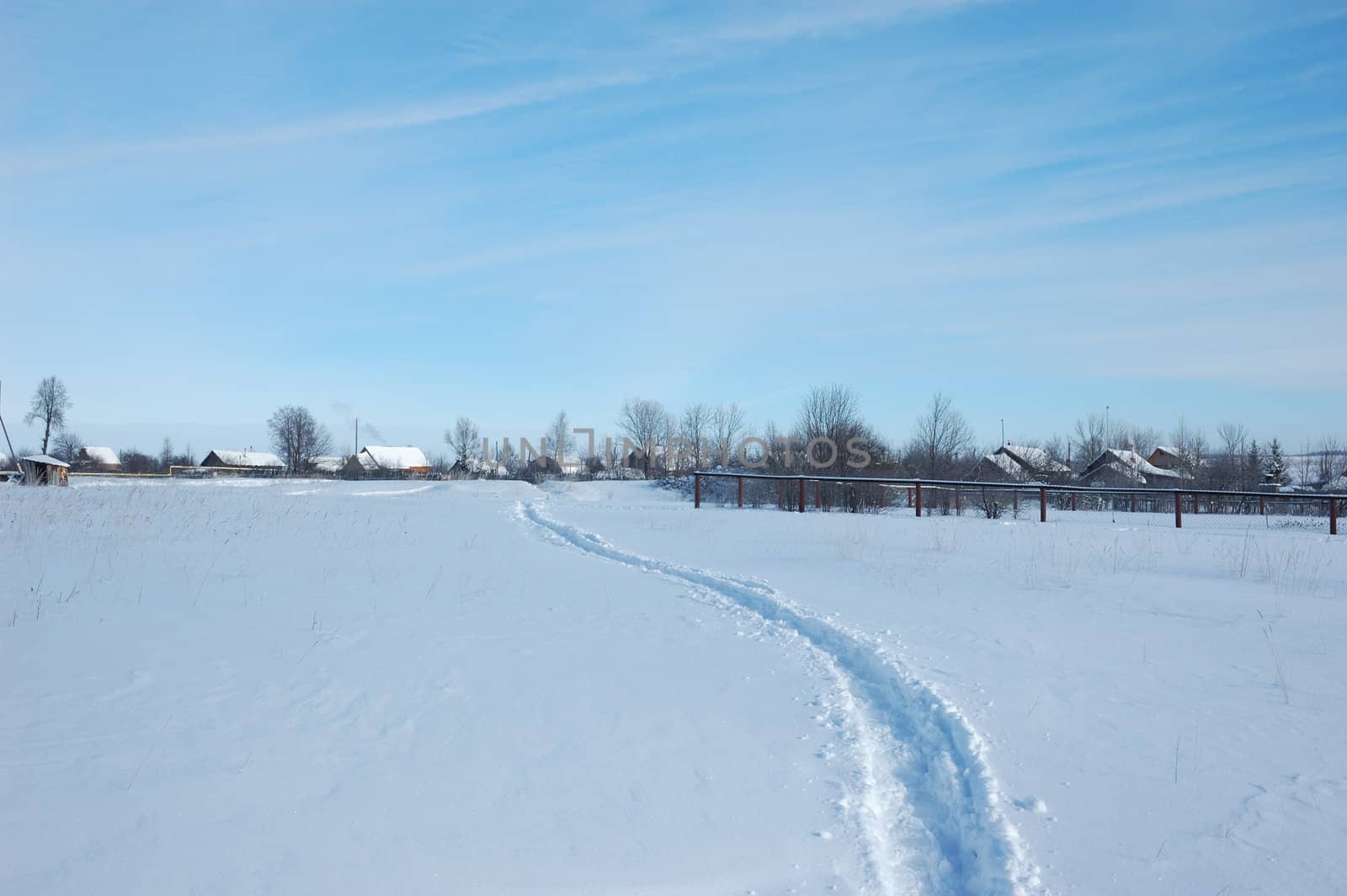 Narrow winter path in field to a small village, sunny winter day
