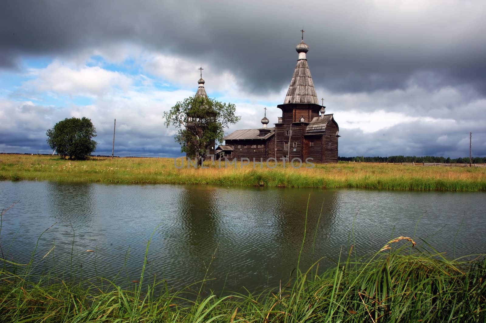 Ancient wooden russian church beyond the river, storm-clouds in sky, north Russia