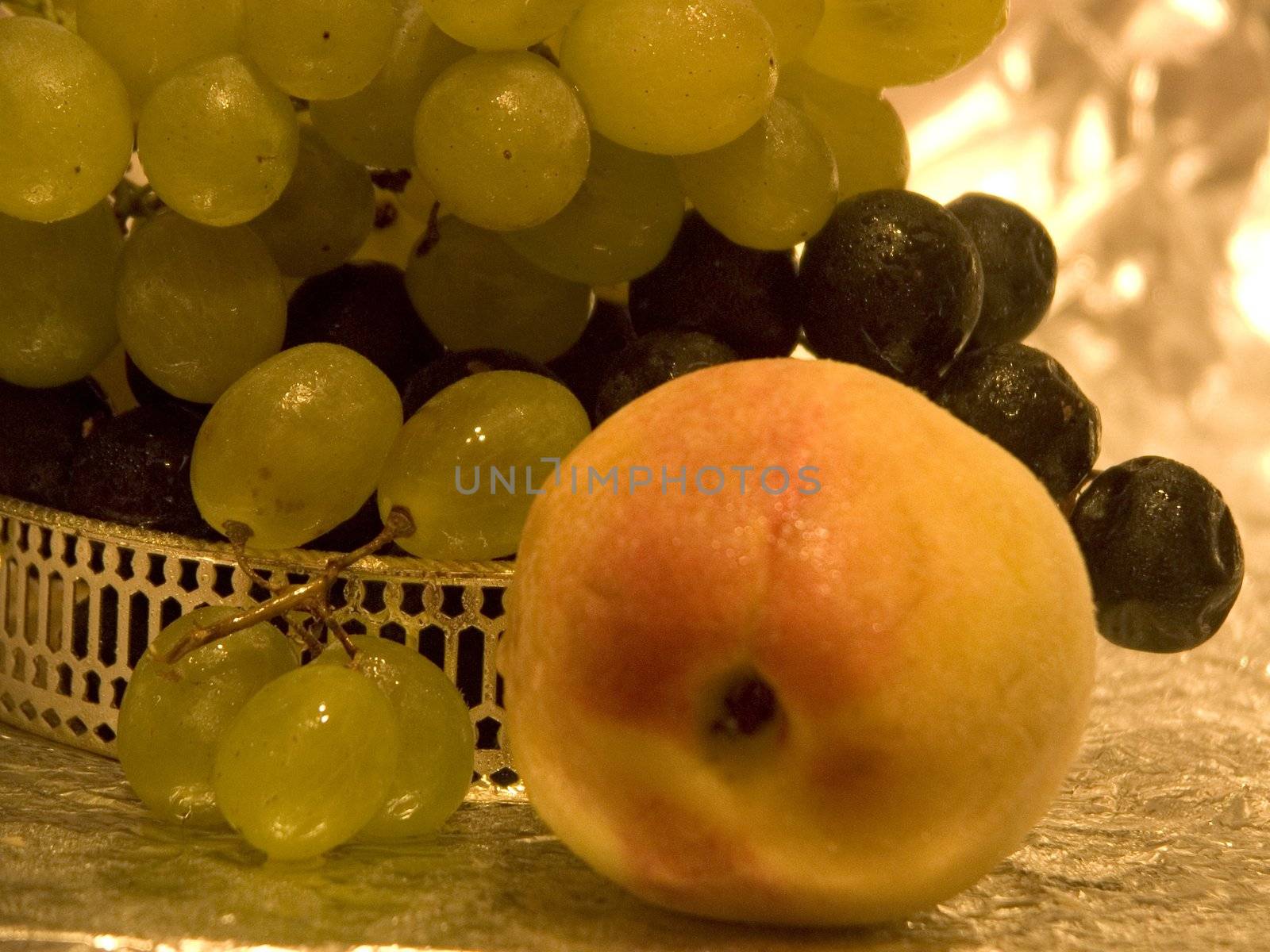 Two kinds of grapes in a silver bowl and a peach in the foreground in golden light
