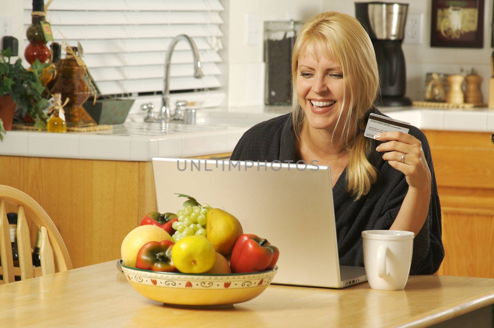 Woman holding credit card in her kitchen Using her Laptop for Ecommerce.