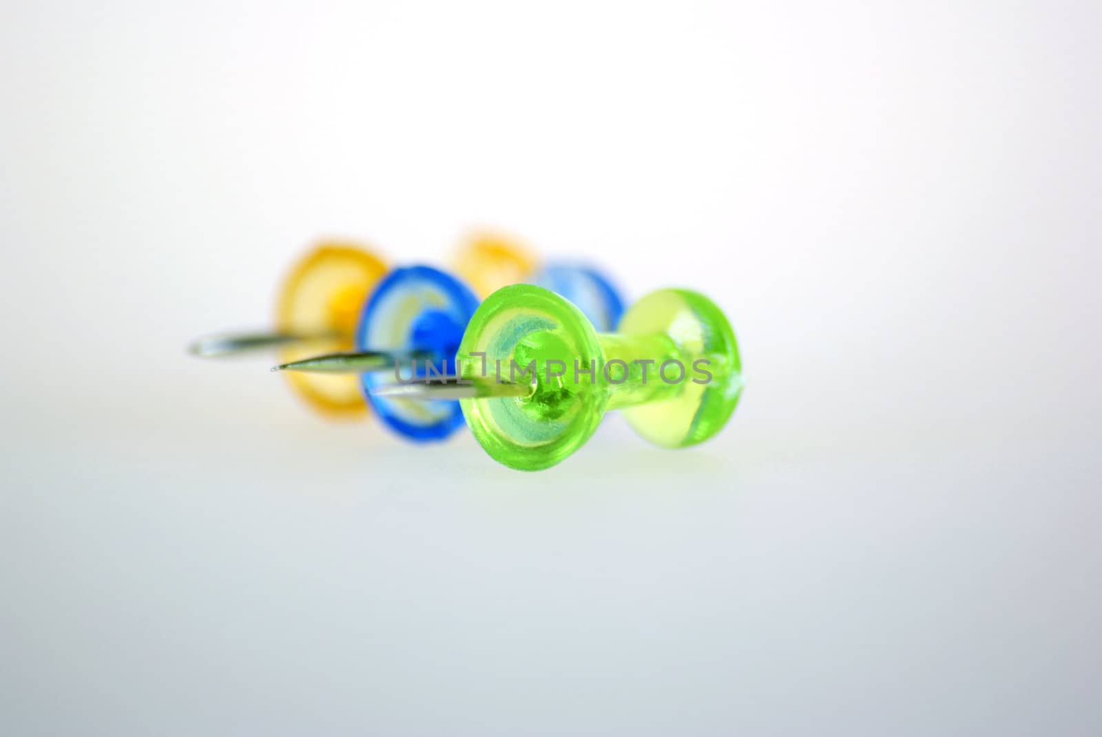 Orange, blue and green transparent drawing pins on grey background.