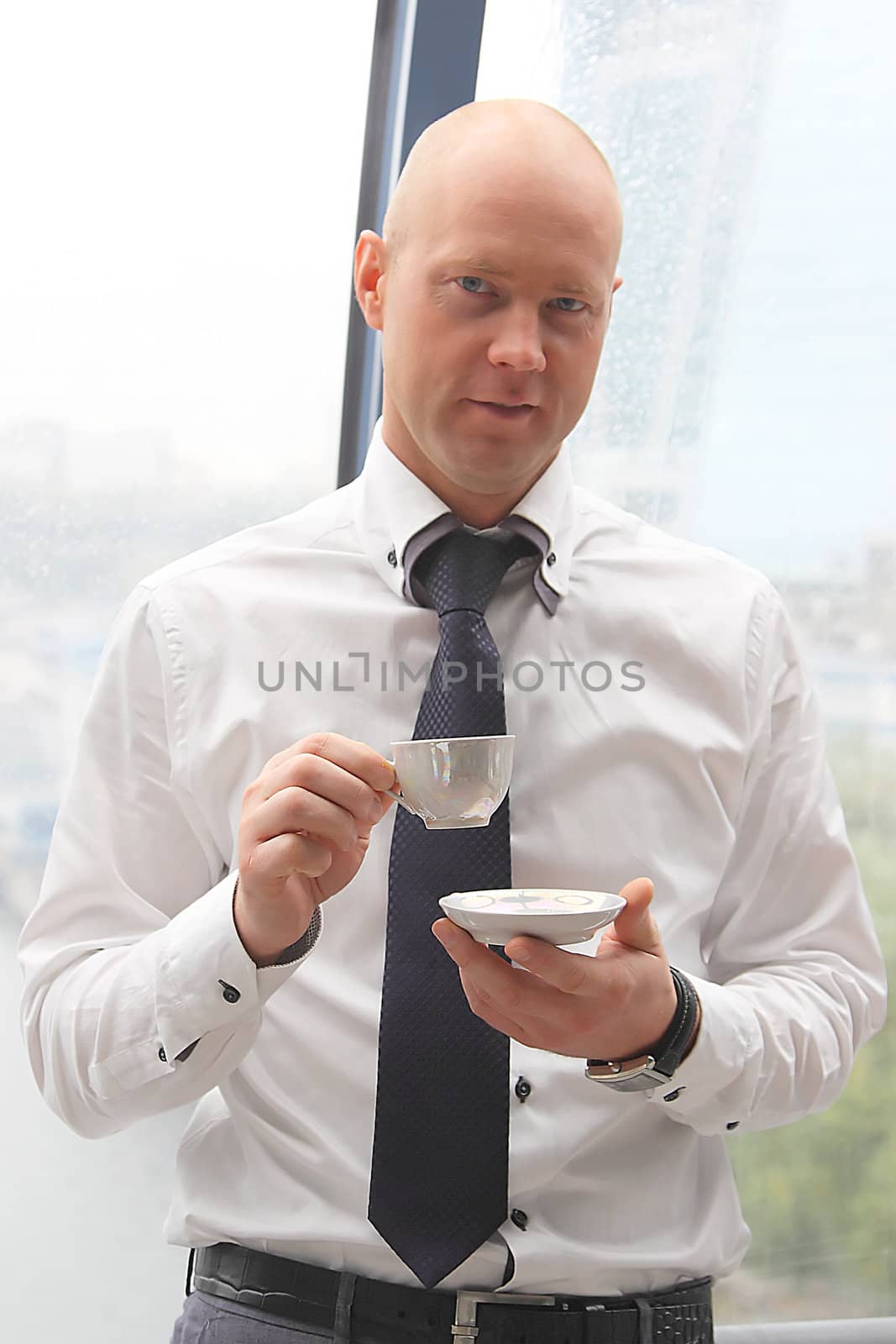 The businessman drinks coffee at office from a small white cup