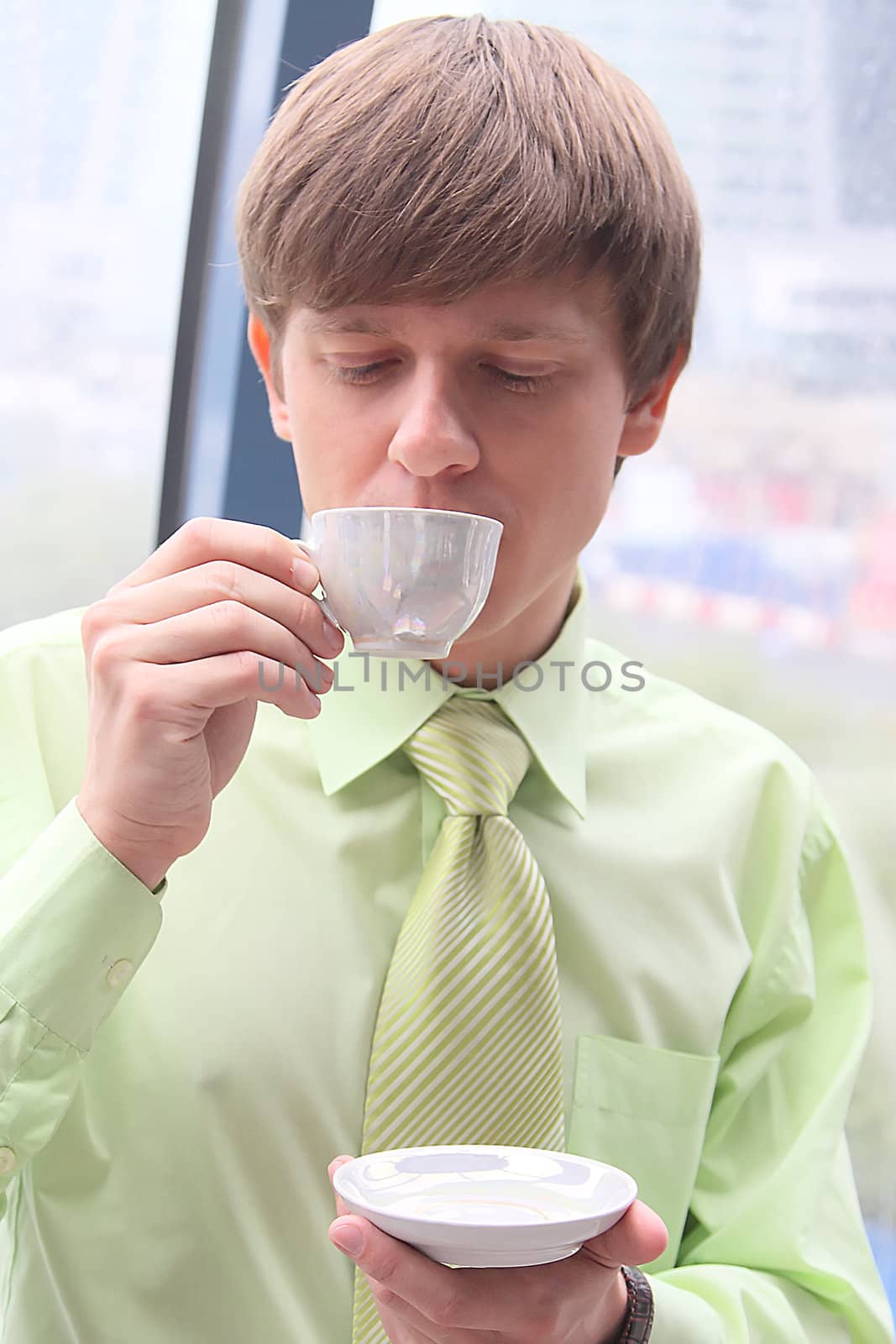 The businessman drinks coffee at office from a small white cup