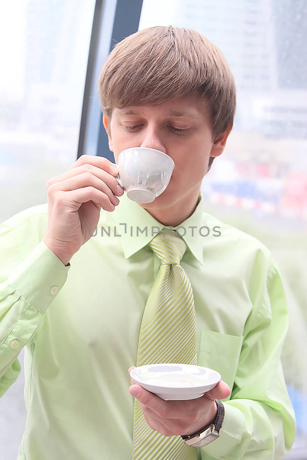 The businessman drinks coffee at office from a small white cup