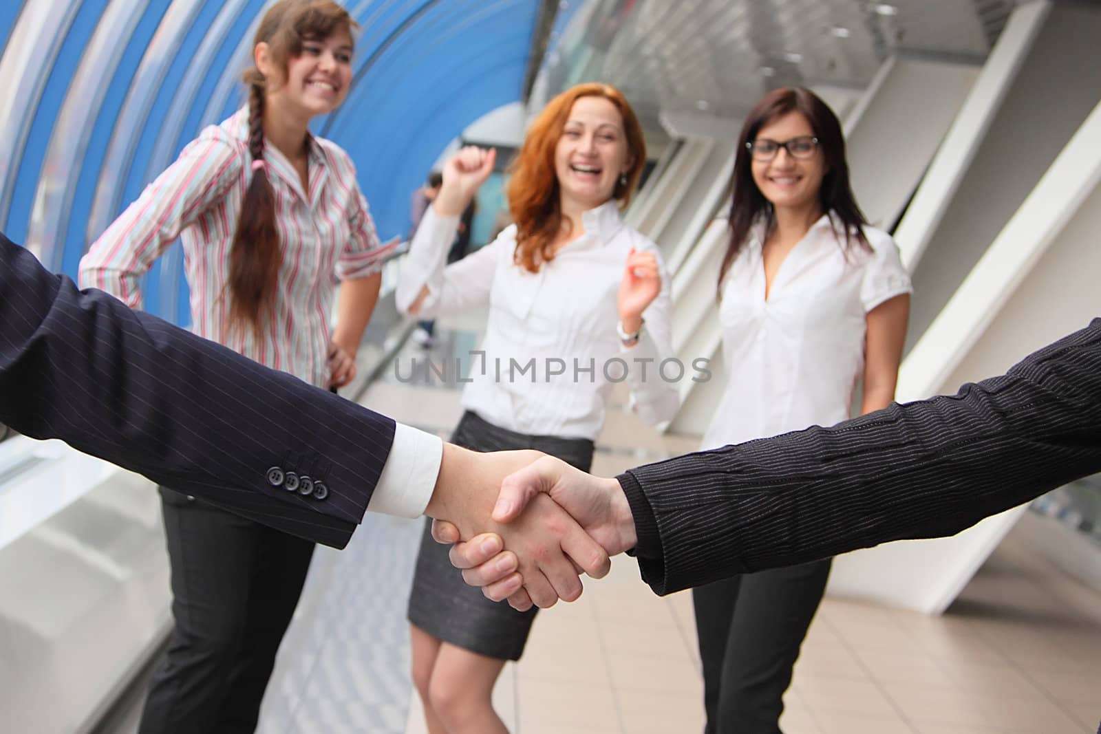 Hand shake of two businessmen against happy colleagues
