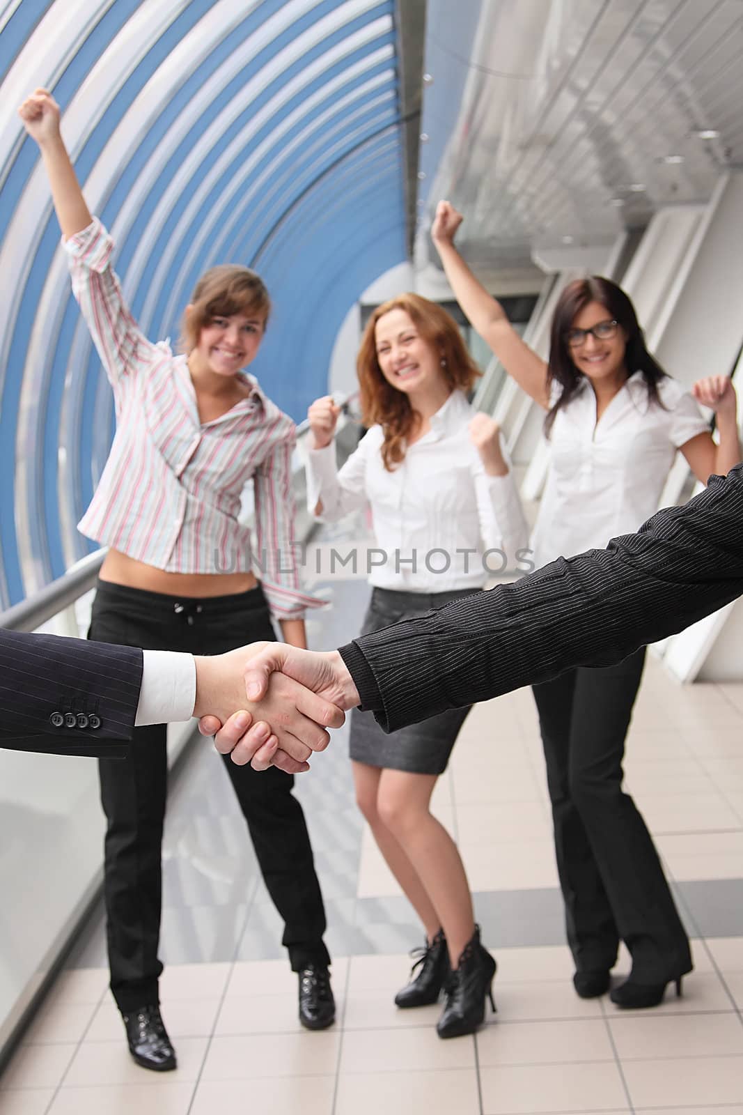 Hand shake of two businessmen against happy colleagues