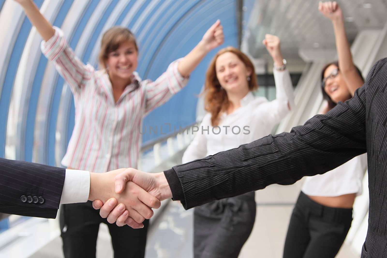 Hand shake of two businessmen against happy colleagues