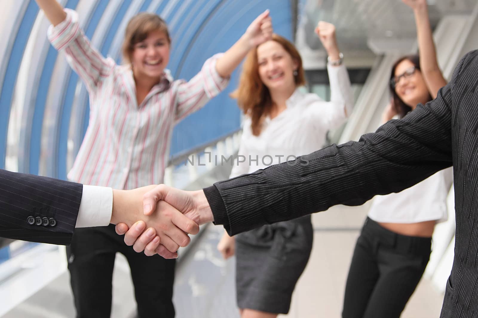 Hand shake of two businessmen against happy colleagues