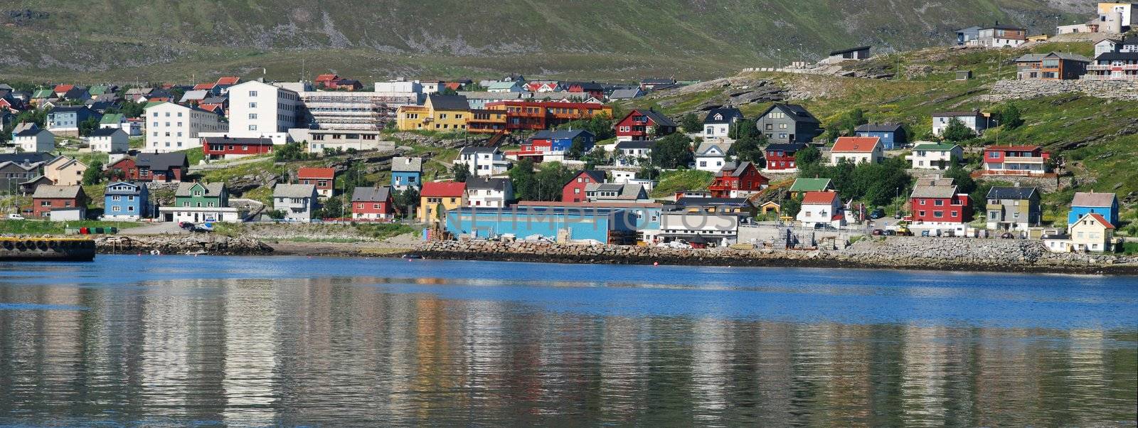 Its a cityscape of Hammerfest, claimed as a northernmost city in the world, the top of city church is behind of houses colored with different colours of Finnmark country and old vessel in the border of see