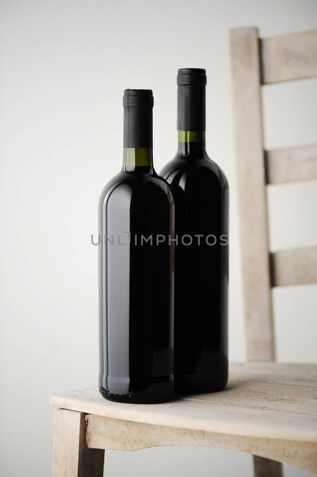 two bottles of red wine on a white wooden chair, on a light background