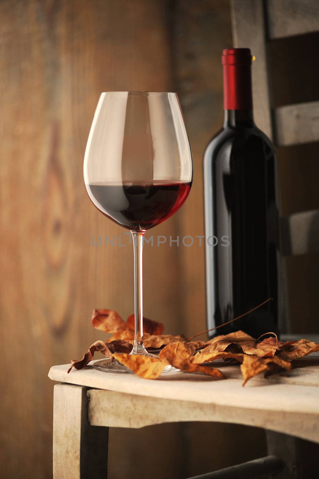  glass of red wine on a wooden chair, with dry leaves and a bottle of red wine on background