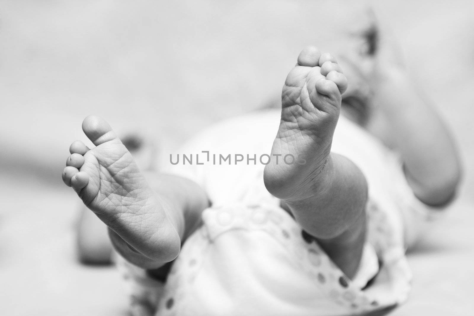 Newborn happy cute baby feet with toes and wrinkles. Infant child laying on back.