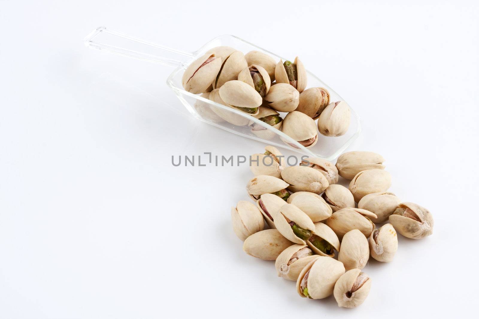 a scoop of roasted and salted pistachio nuts on white background