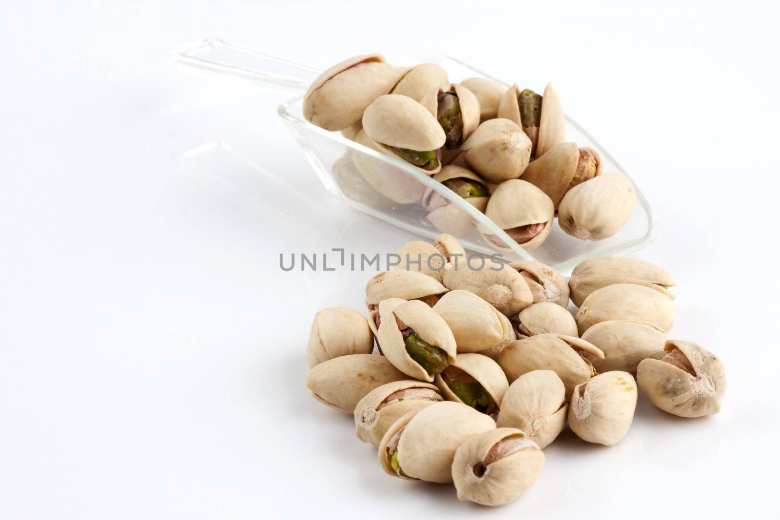 a scoop of roasted and salted pistachio nuts on white background