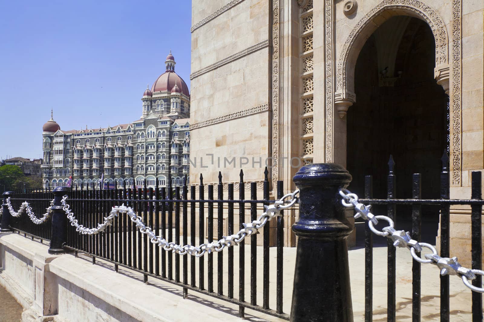 Landscape of the Gateway of India, its black and silver painted railings with a cameo view of the Taj Hotel with an angled view of an archway