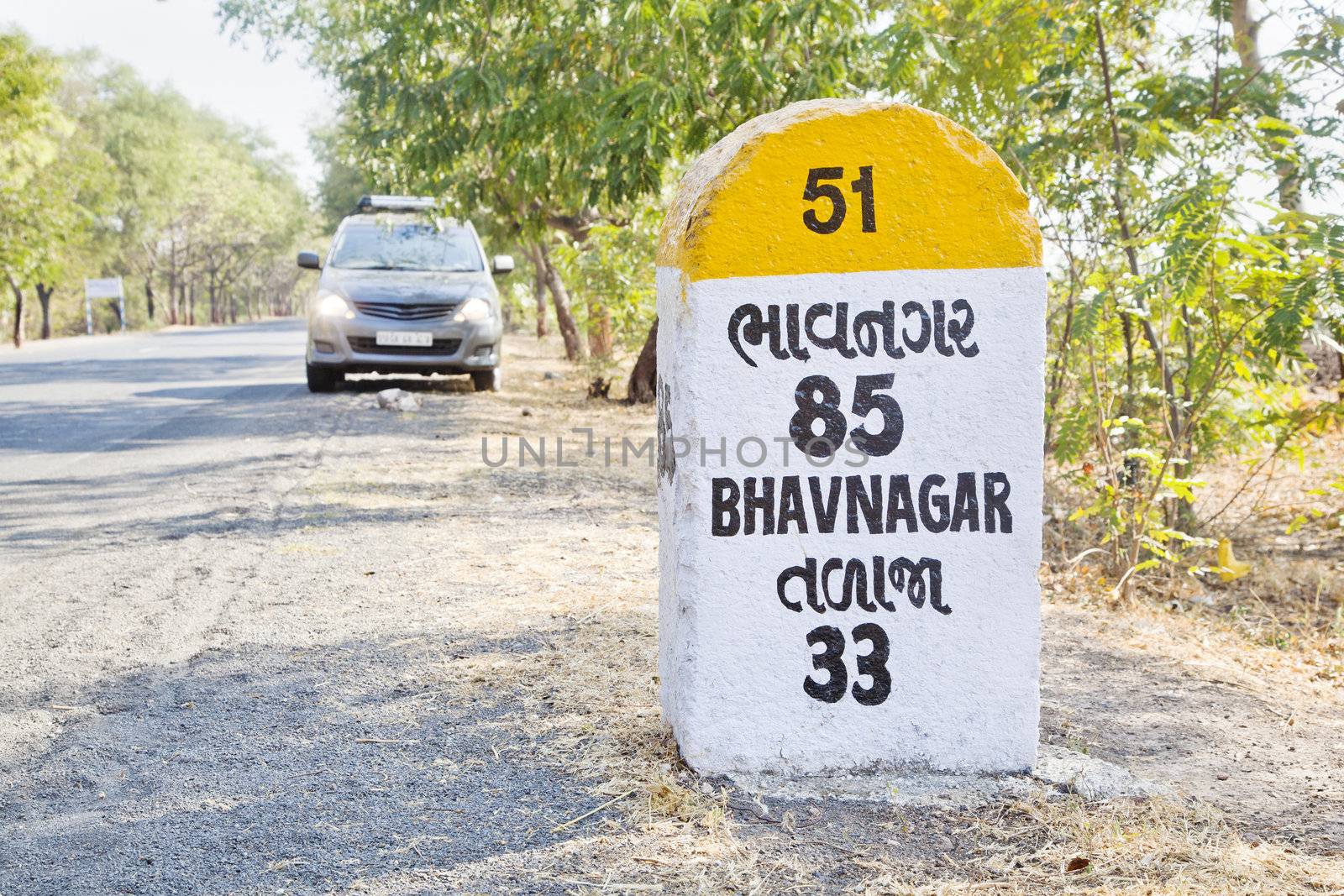 Horizontal rural landscape in Gujarat India incorporating 85 kilometers to Bhavnagar milestone and land mark on the coastal road to Dwarka a religious town for Hindus. Parked people carrier with head lights switched on