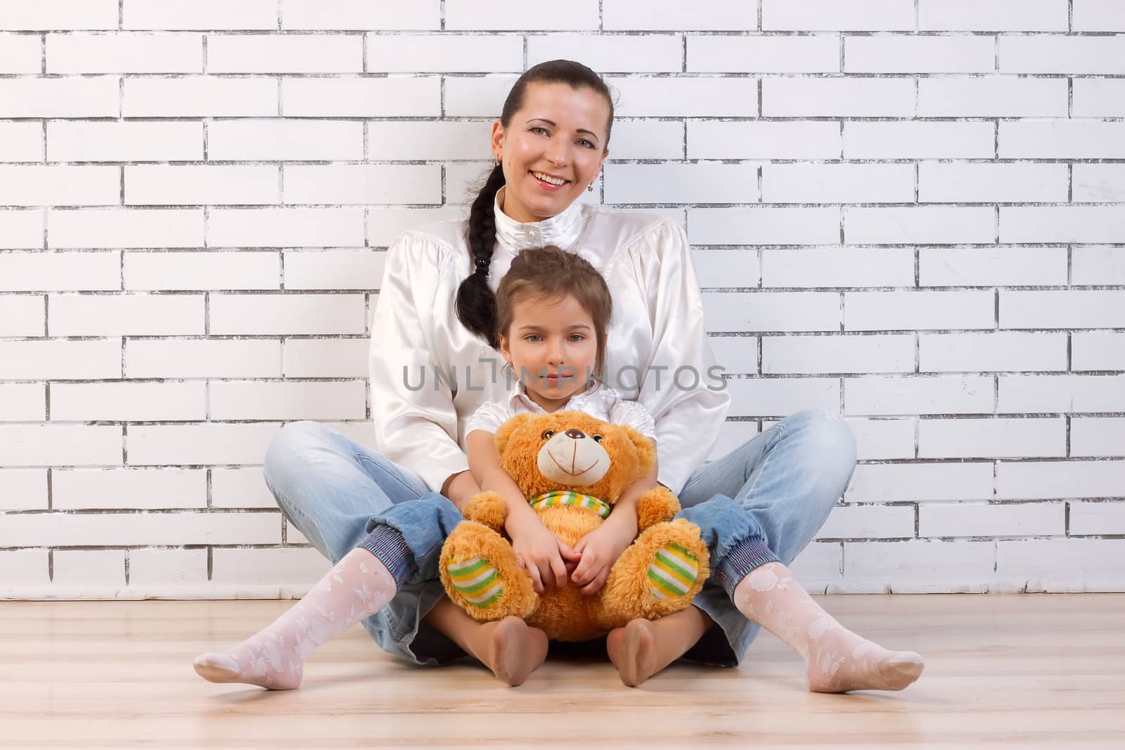 Mother, daughter and soft toy sitting near the wall