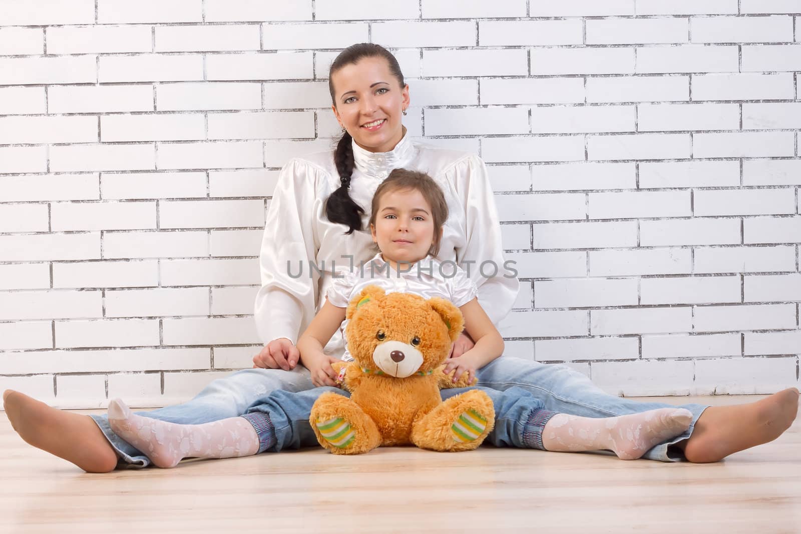 Mother, daughter and soft toy sitting near a white wall