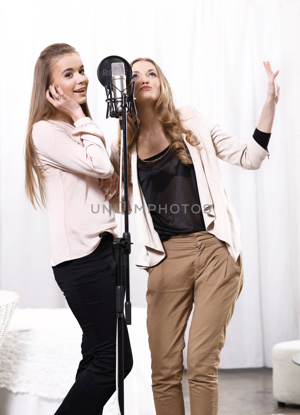 Two girls singing around the microphone in the studio by robert_przybysz