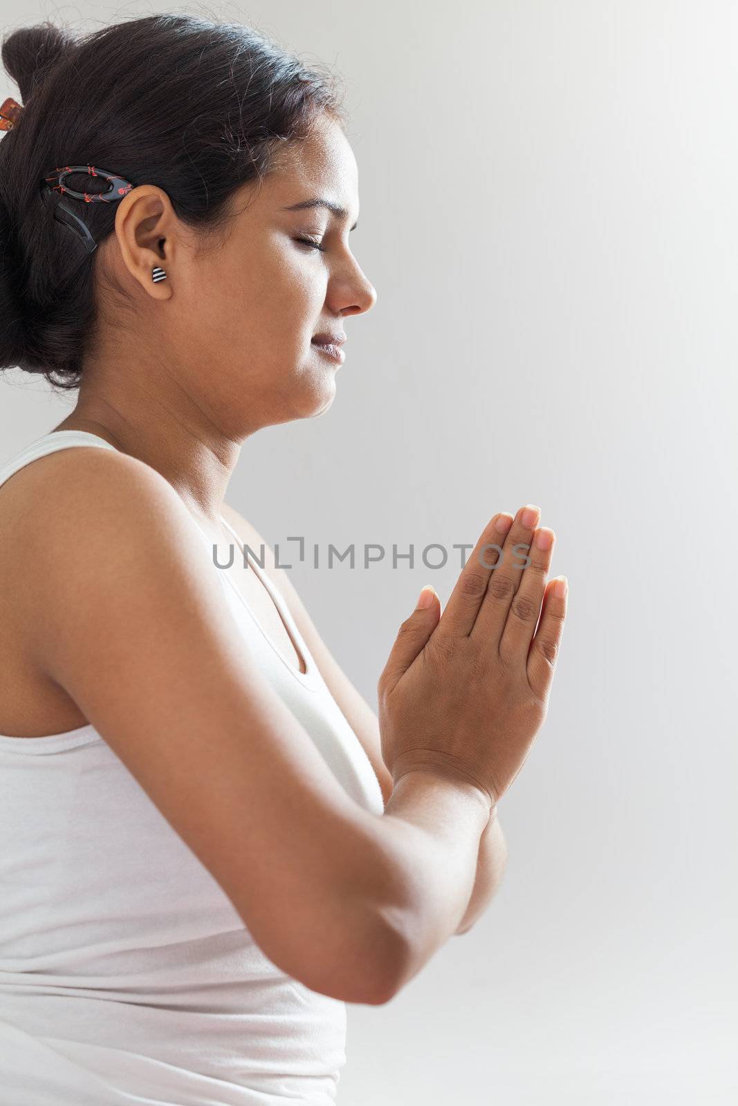 A beautiful Young Indian girl in white top doing meditation by joining hands