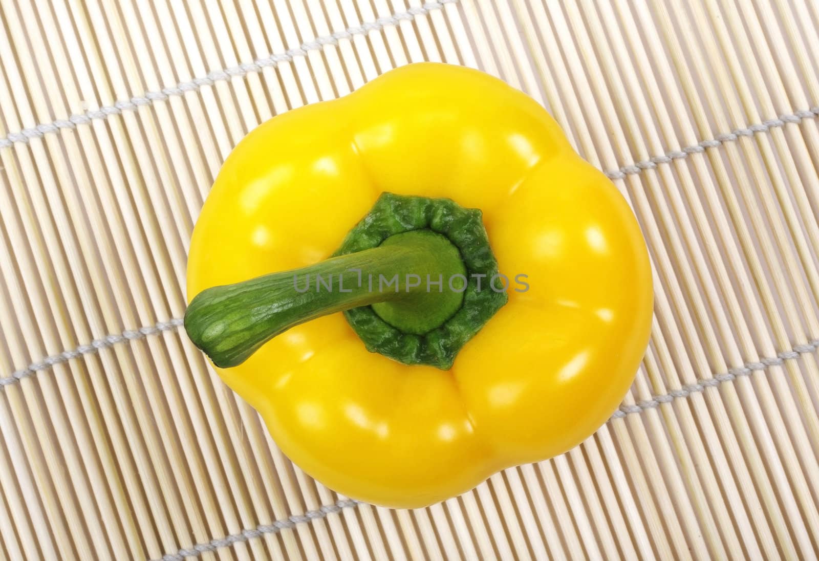 Yellow bell pepper with green stem laying on asian wooden mat.