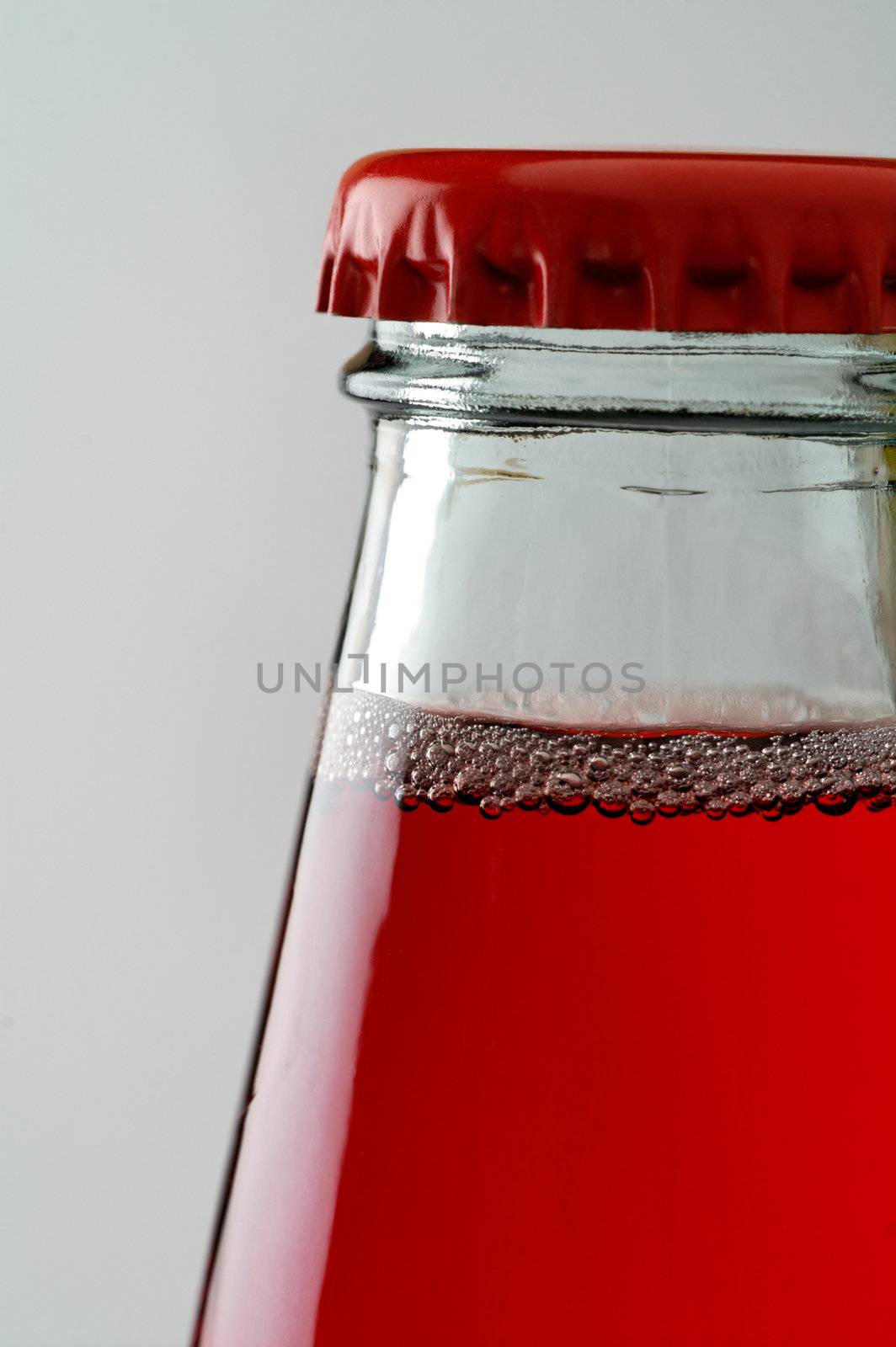 Red drink with bubbles in bottle closed with red crown cap