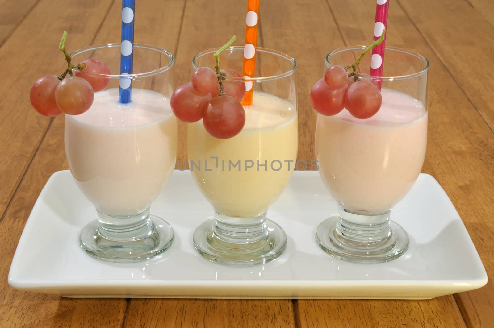 Smoothies with colored drinking straws decorated with grape on a serving dish