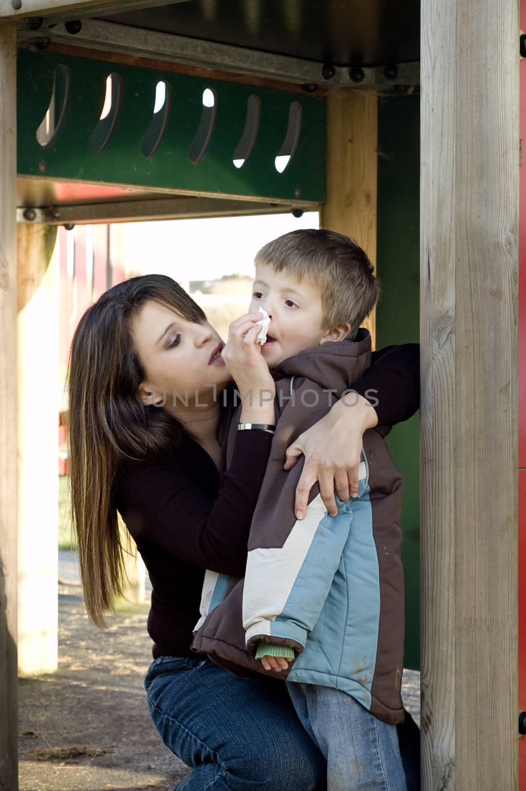 Mum caringly wipes her son's nose in a playground