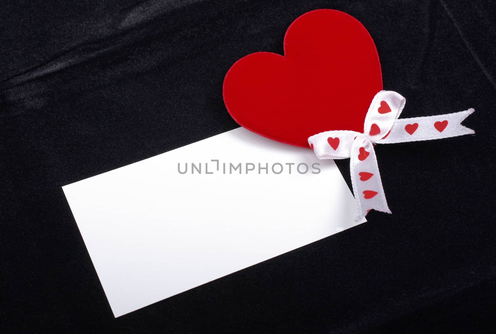 Red heart and white card macro isolated on black velvet background. Empty space for your design.